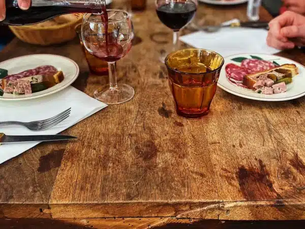 Ambiance conviviale autour d’un déjeuner dans un bouchon lyonnais, charcuterie et vin rouge à table.