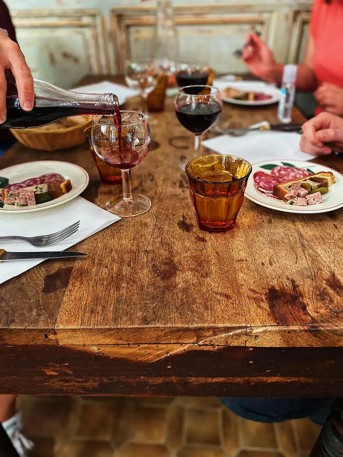 Ambiance conviviale autour d’un déjeuner dans un bouchon lyonnais, charcuterie et vin rouge à table.